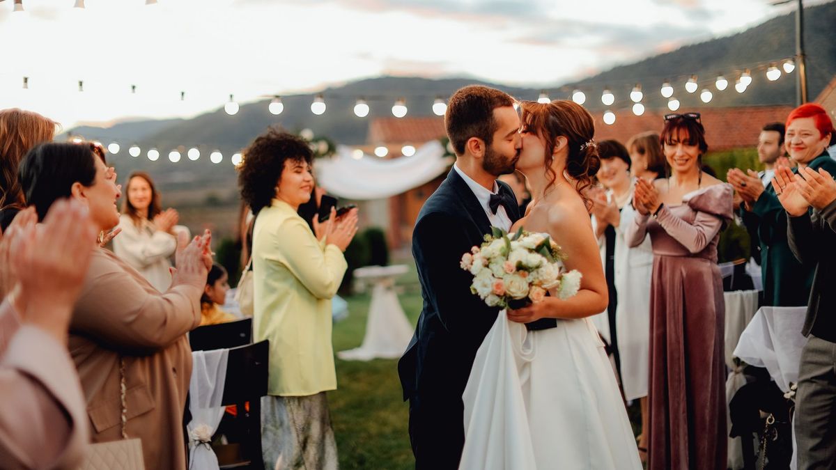A couple kissing as their guests applaud around them